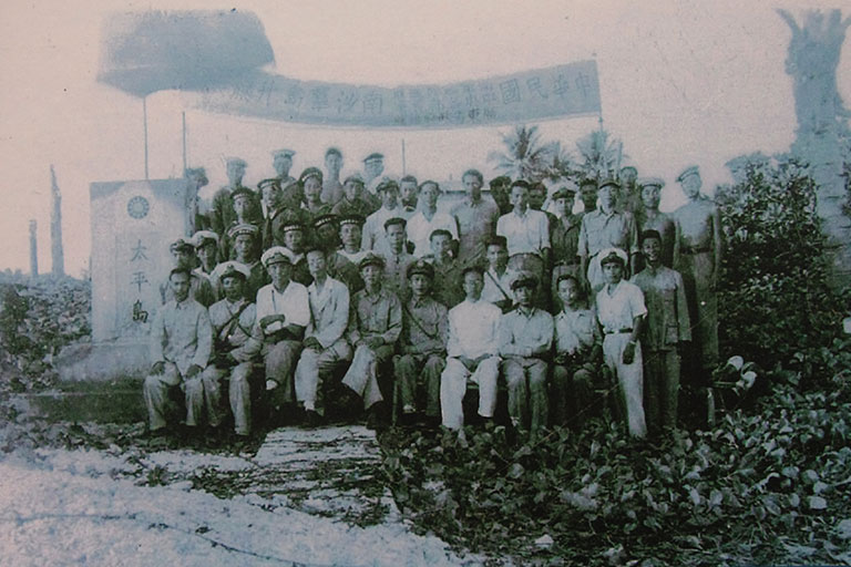 圖四 民國35年中華民國海軍收復太平島。太平艦12月12日駛抵該島後,官兵在島上升旗立碑,相片中前排左四為內政部代表鄭資約,左五為支隊指揮官林遵。太平艦全艦官兵約有180人,所以照片中人只是其中的少數。(來源:維基共享資源,公有領域)